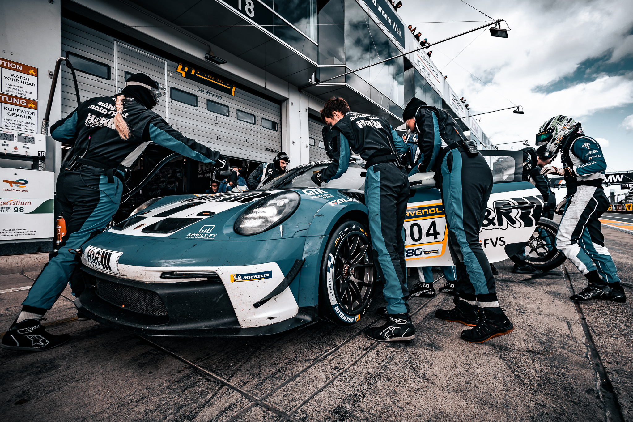 Boxencrew arbeitet beim Boxenstopp an einem türkisfarbenen Porsche mit der Startnummer 04
